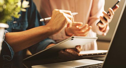 Zwei Personen zeigen etwas auf ihrem Tablet bzw. Smartphone